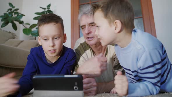 Grandchildren teaching to his grandfather to use tablet. Home comfort. Family idyll.