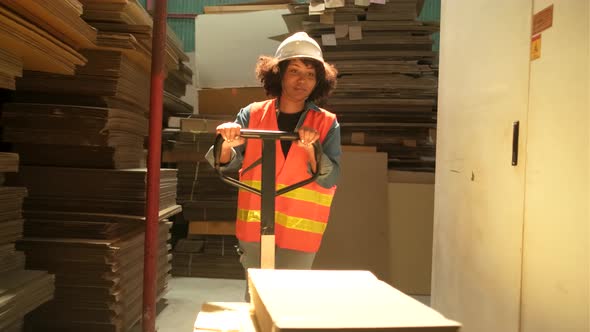 A female worker hauls hydraulic trolley piles of cardboard for logistic transport.