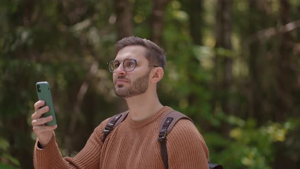 A Young Man Wearing Glasses Tourist with a Beard Shoots Video on the Phone of His Journey in Slow