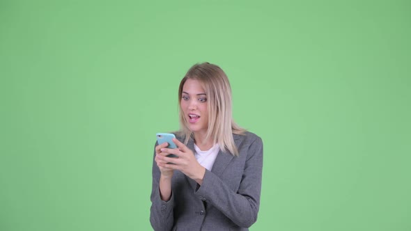 Face of Happy Young Blonde Businesswoman Using Phone and Looking Surprised