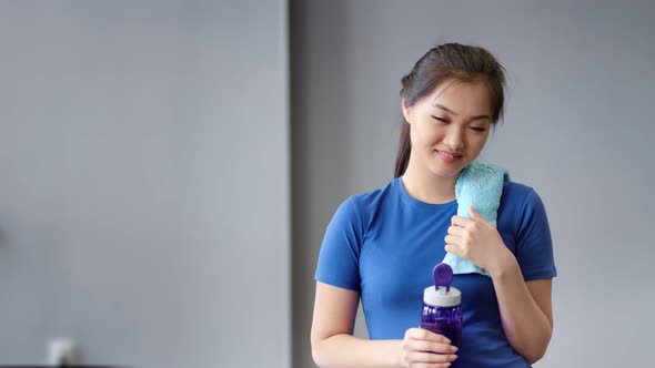 Portrait Smiling Asian Female Fitness Instructor Holding Bottle of Water and Towel Looking at Camera