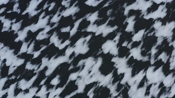 Snow deposits across sheet of ice on lake ascending aerial