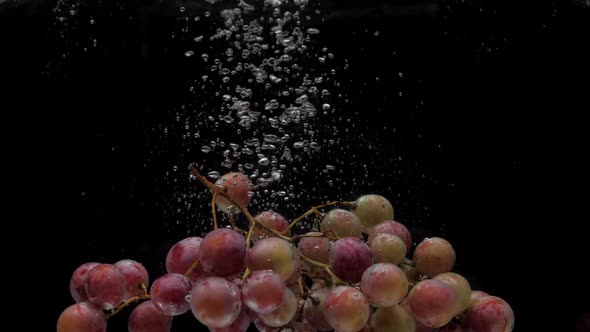 Slow Motion Red Grapes Falling Into Transparent Water on Black Background