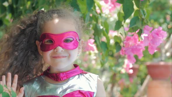 Beautiful Llittle Girl in the Superhero Costume, Dressed in a Pink Cloak and the Mask of the Hero