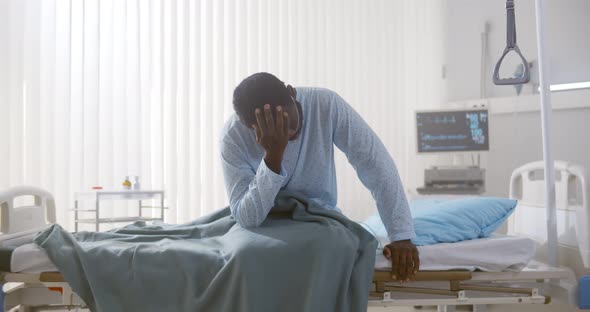 Portrait of Afroamerican Sick Patient Sitting on Hospital Bed and Rubbing Face