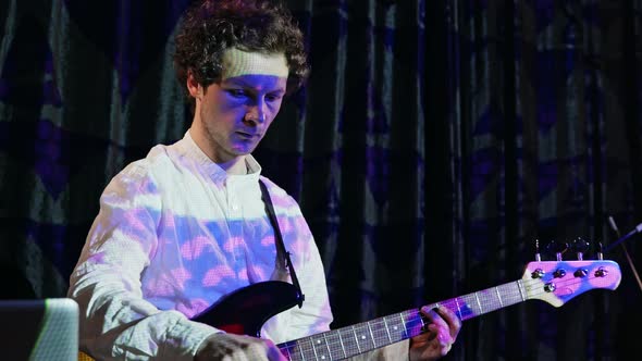 Curly Male Musician Playing Bass Guitar and Mixing Music in the Club