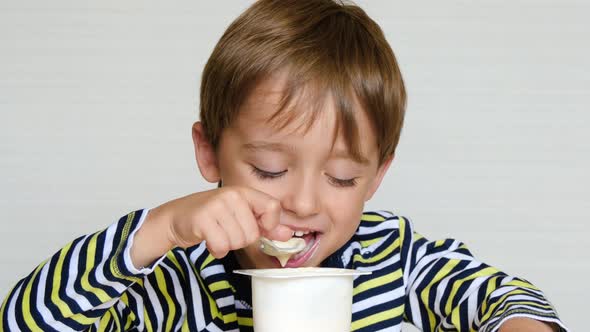 A Cute Little Boy of European Appearance Is Sitting at the Table and Eating a Dairy Product. Child