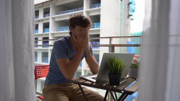 Young Man Sitting on a Balcony with a Notebook and Suffering From a Loud Noise