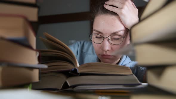 A young girl with glasses falls asleep over a textbook late in the evening