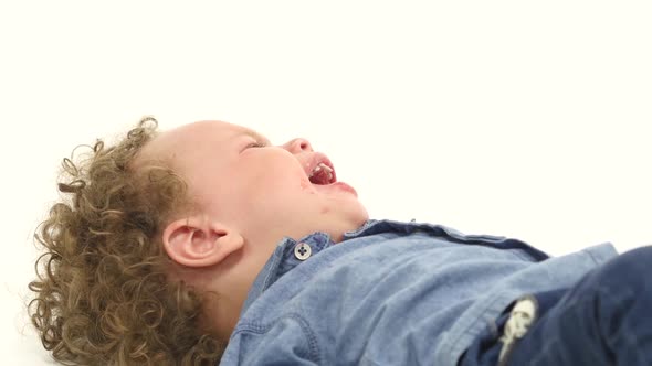 Little African American Boy Lies on the Floor and Cries, He's Upset. White Background alt