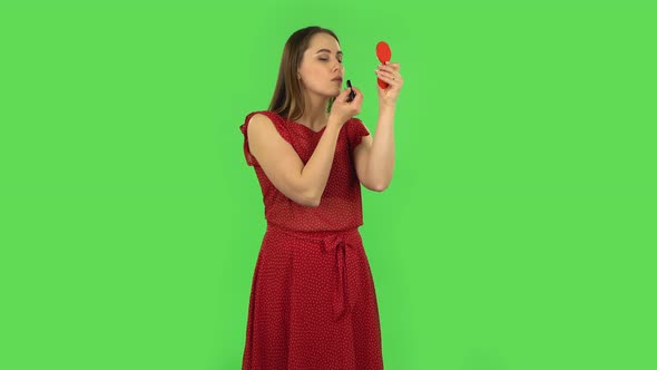 Tender Girl in Red Dress Is Painting Her Lips Looking in Red Mirror. Green Screen