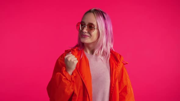 Girl with pink hair and extraordinary appearance shows yes gesture of victory, she achieved result