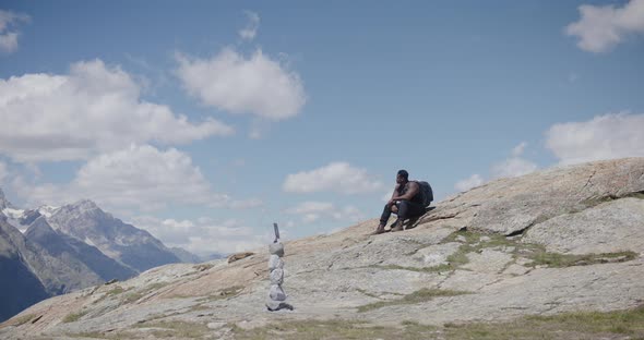 Black male traveler with backpack walking up scenic mountainside edge and resting near the Matterhor