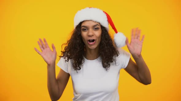 Happy Biracial Woman in Santa Claus Hat Jumping Out, Smiling at Camera, Greeting