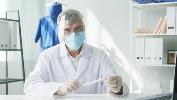 PCR Test in Laboratory Aged Doctor in Glasses Holding COVID19 Swab Collection Kit and Looking in