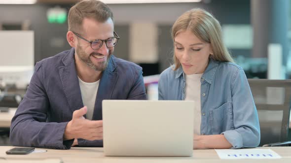 Middle Aged Man and Young Woman Doing High Five While Using Laptop