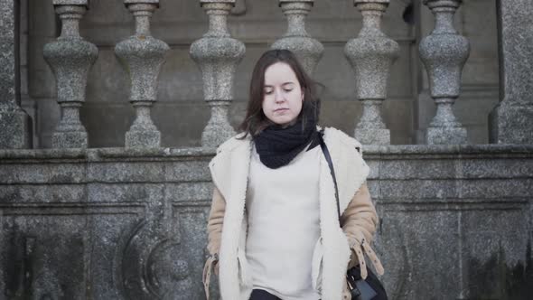 Young female tourist in warm clothing walking down steps in front of historical building, slow motio