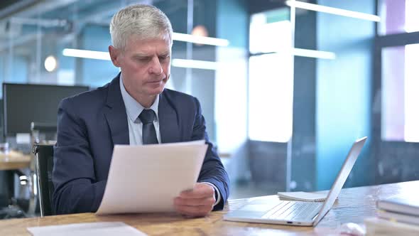 Middle Aged Businessman Reading Document on Office Desk