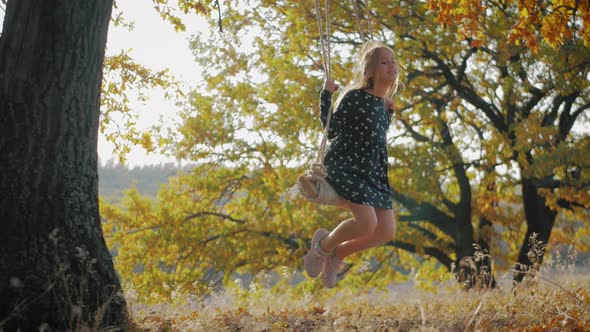 Happy Child Girl on Swing at Golden Sunset