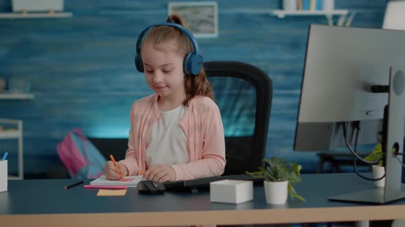 Young Child Wearing Headphones and Drawing on Textbook