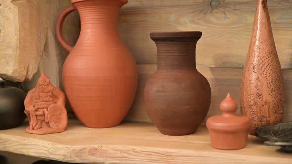 A view of an earthen pot that sits on a wooden shelf among other earthen pots
