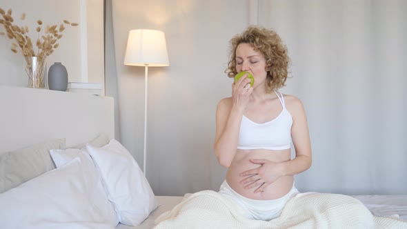 Healthy Pregnant Woman Eating Green Apple In Bed