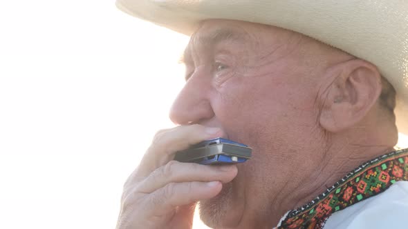 Closeup of the Face of an Old Man in a Hat Playing the Harmonica