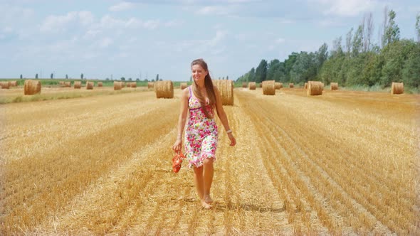 Girl Walks on the Cultivated Field with Haystacks