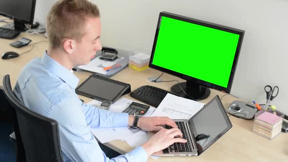 Young Handsome Man Works on Laptop Computer in the Office - Green Screen - Computer and Tablet