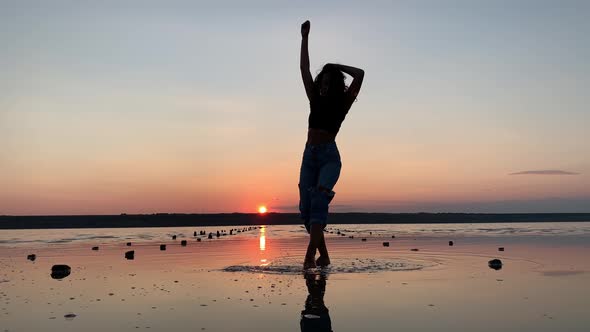 Silhouette of a beautiful woman dancing in the background of the sunset in the water.