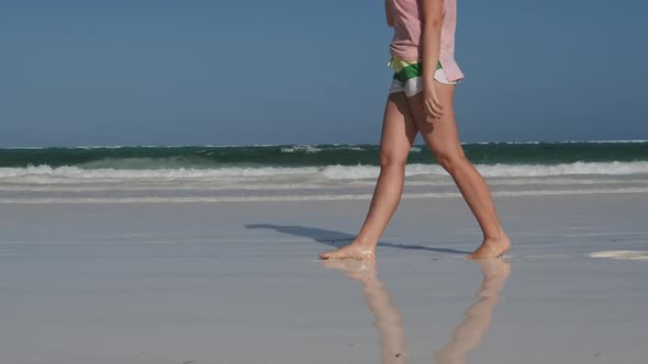 Legs of Young Woman Walking By White Sand Paradise Beach with Tidal Ocean Waves