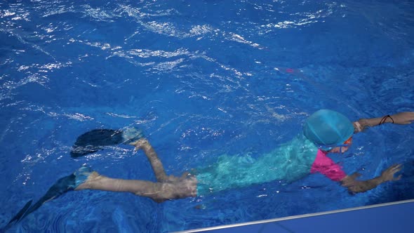 Little Girl in Swimsuit Cap and Goggles is Diving and Swimming to Egge of Pool