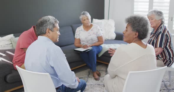 Mixed race senior female counsellor with clipboard advising to group of diverse senior friends