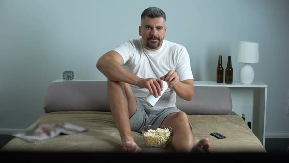 Bachelor Spending Evening Home in Front of TV, Drinking Beer and Eating Popcorn