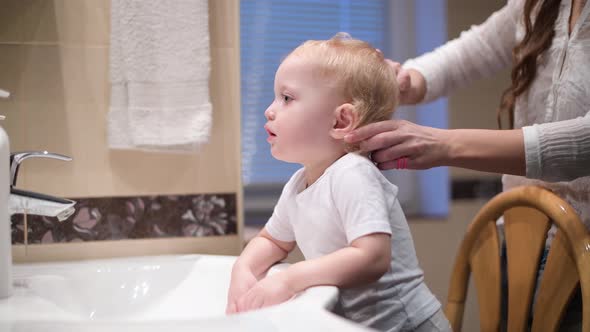 mom comb the hair of her little daughter in front of the bathroom mirror