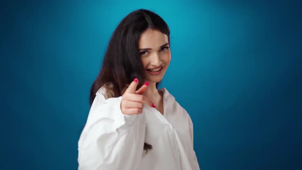 Friendly Smiling Young Woman Pointing to Camera Against Blue Background