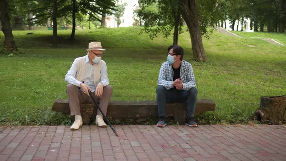 Old Man Sitting with His Young Acquintance in Medical Masks and Talking to Each Other