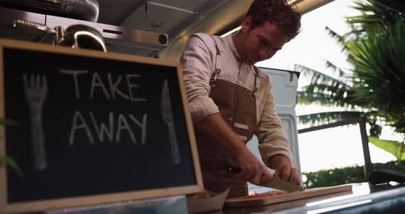 Caucasian male chef working inside food truck preparing dinner food - Summer job concept