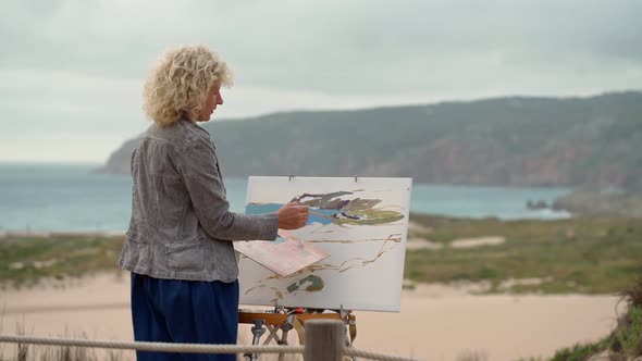 A Middleaged Woman Artist By the Sea Draws a Beautiful Sketch of a Picture of a Sea Beach with