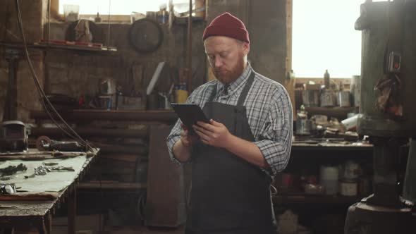 Blacksmith Using Digital Tablet in Workshop