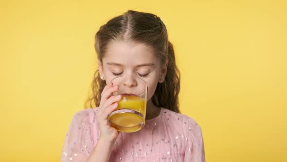 Beautiful Kid Girl Drinking Orange Juice From Glass at Yellow Background.