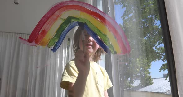 Young Schoolboy in Yellow Tshirt Draws Rainbow on Window