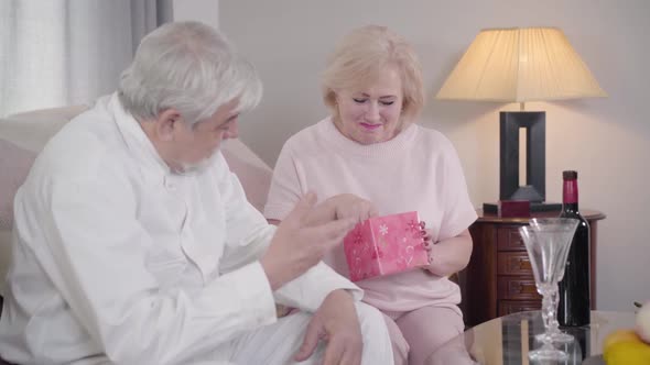 Portrait of Surprised Caucasian Senior Woman Opening Gift Box. Wife Receiving Elegant Scarf on Saint