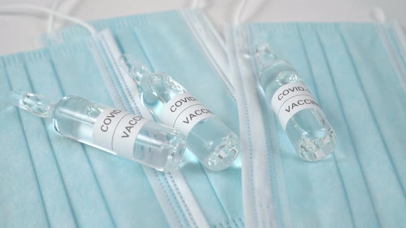 Glass ampoules with a clear liquid called COVID-19 VACCINE on blue protective medical masks