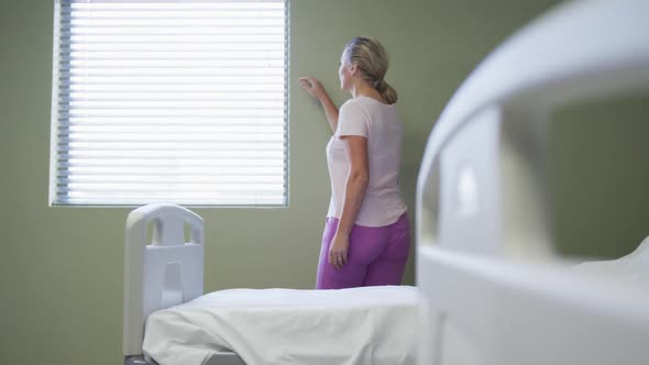 Caucasian female patient standing in hospital room looking at window