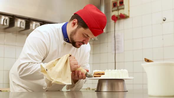 Pastry chef at work in a cake shop preparing and decorating a cake with whipped cream