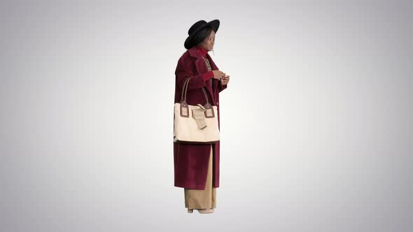 African American Fashion Girl in Coat and Black Hat Posing with a Handbag on Gradient Background