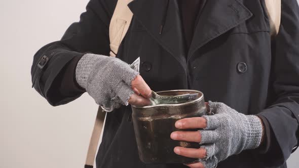 Close Up of a Homeless Beggar's Hands Pulling a Paper Bill Out of a Cup To Collect Money.