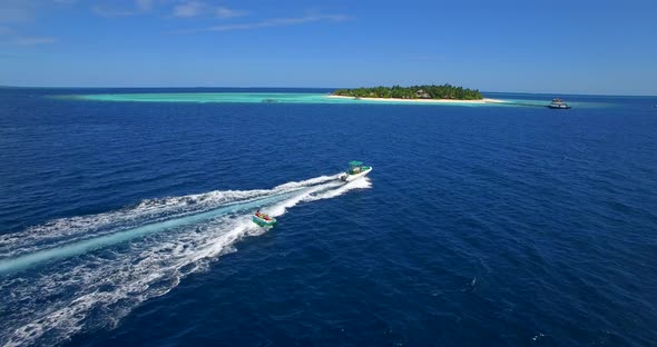 Aerial drone view of man and woman on an inflatable tube towing behind a boat to a tropical island.