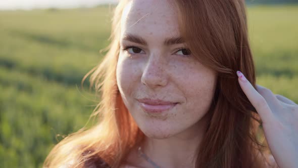 Flirty Girl with Long Red Hair and Freckles Looking in Camera in Summer Day